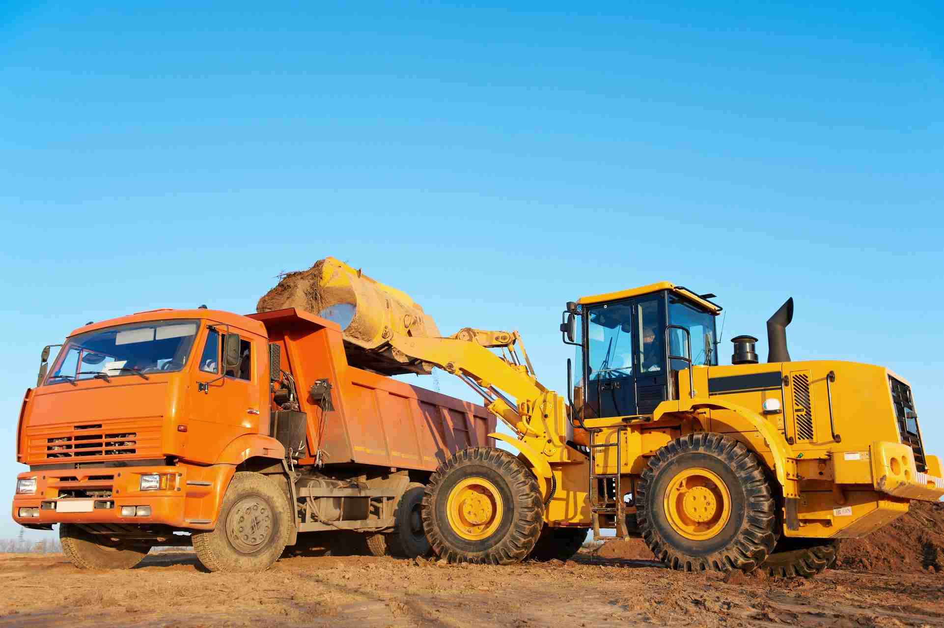 A wheel loader dumping dirt into an orange dump truck
