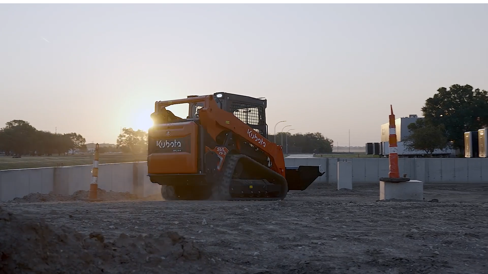 Kubota compact track loader on a graded jobsite at sunrise with traffic cones