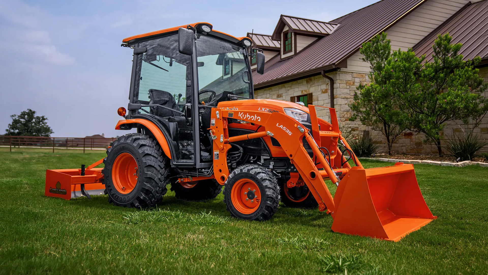 Kubota LX2620 cab tractor with a front loader and rear blade parked in front of a home