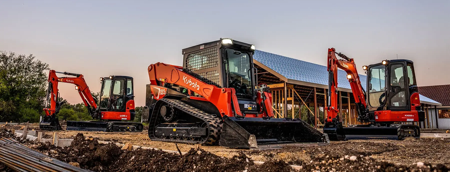 Kubota track loaders and excavators lined up in front of a building