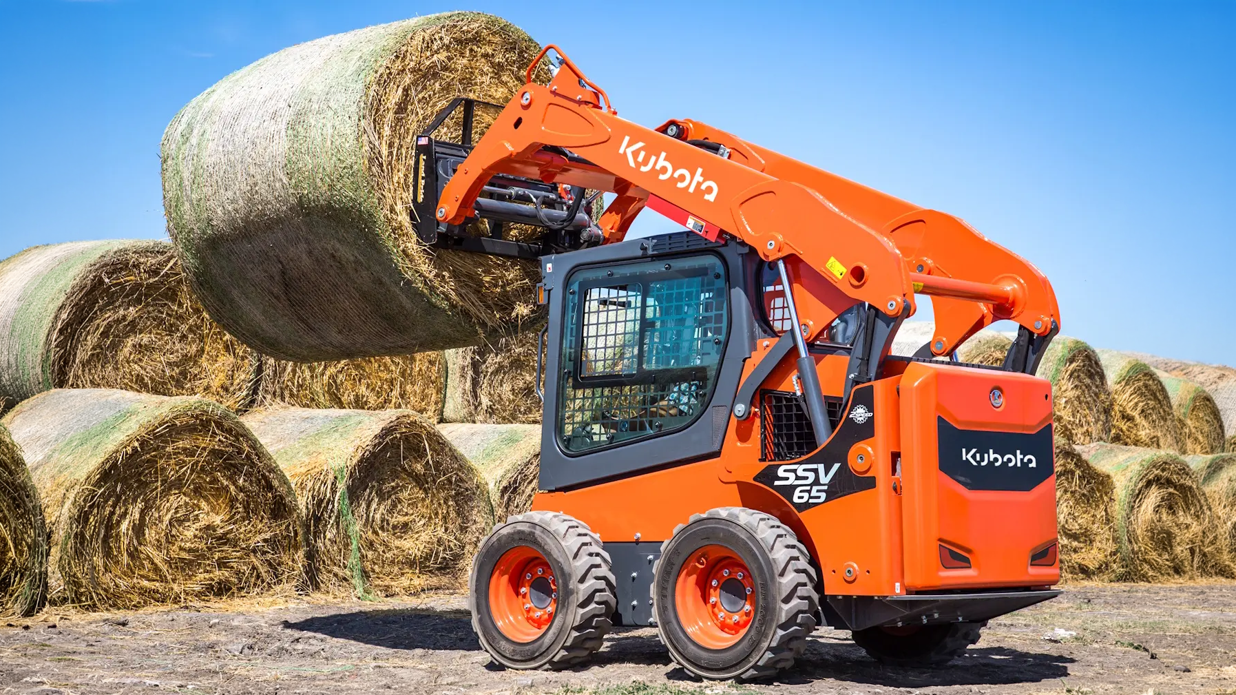 Kubota SSV65 skid steer carrying a round hay bale